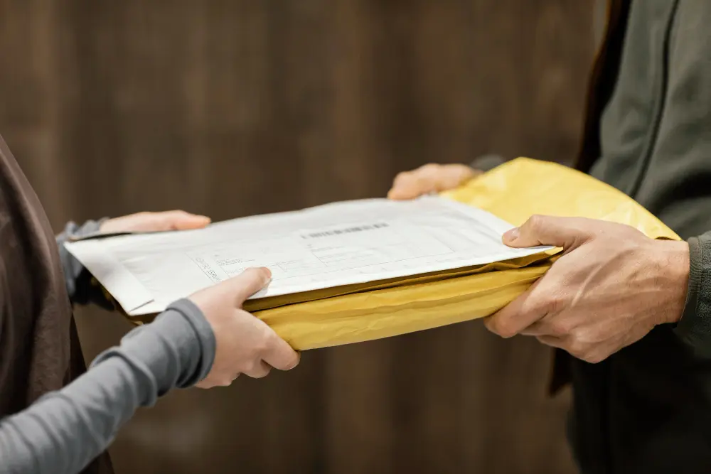 Foto com duas pessoas, com a da esquerda entregando um bloco de documentos de retificação administrativa e judicial para a pessoa da direita