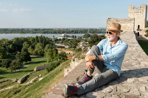 Dante causa: Foto de um senhor idoso sentado em uma muralha de pedra, apreciando a vista da Itália