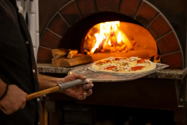 Diferença entre pizza napolitana e romana: foto de um pizzaiolo colocando uma pizza para assar no forno